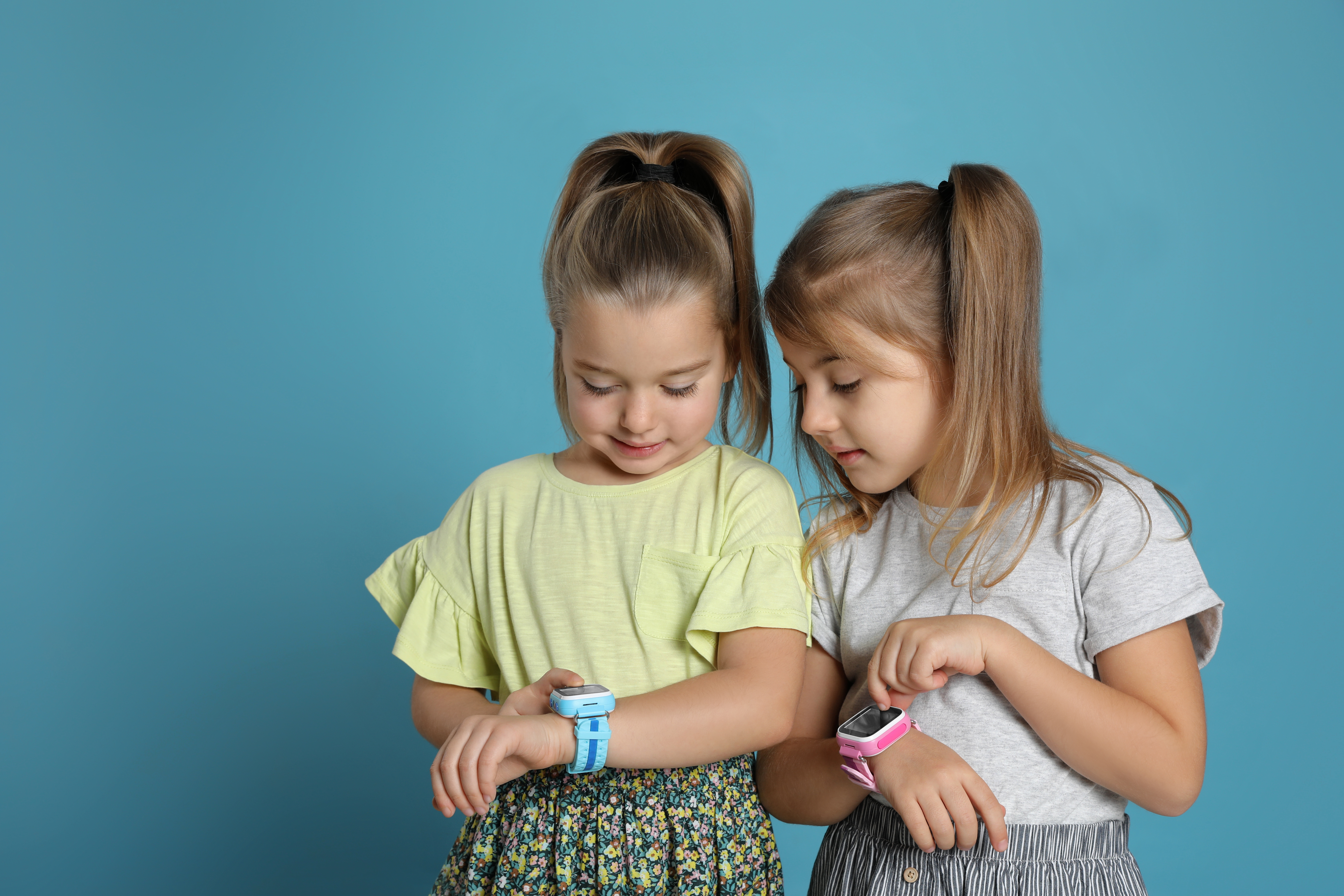 Little girls with smart watches on light blue background